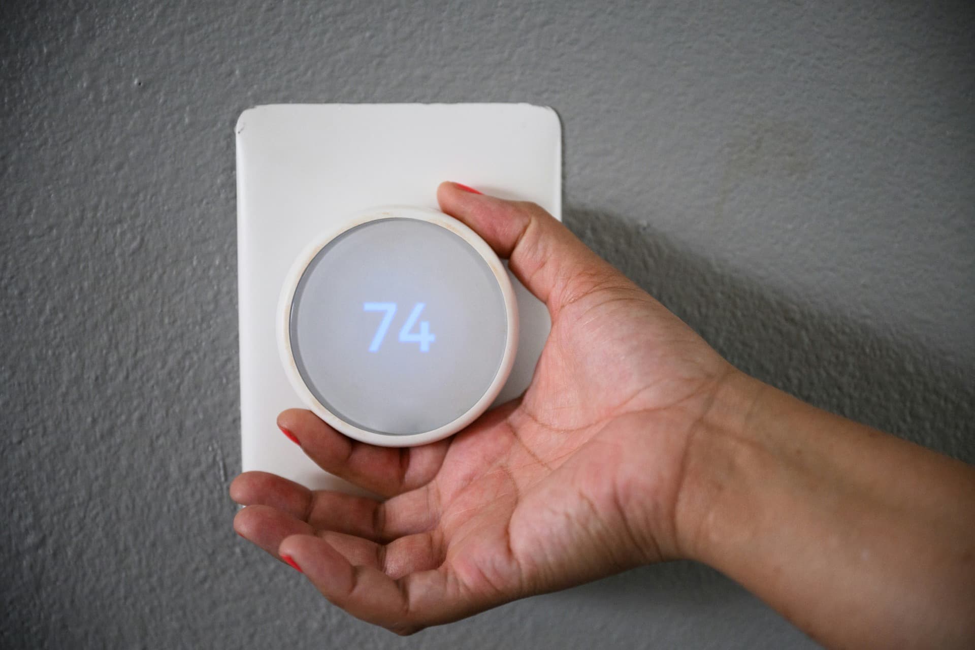 Hand adjusting a smart thermostat on a wall.